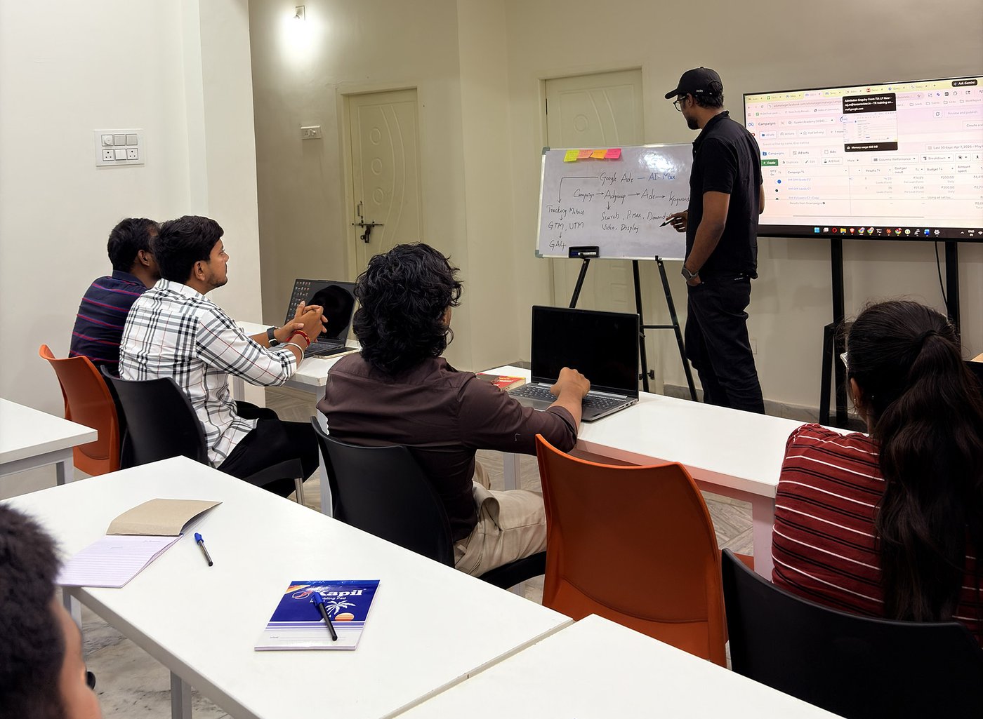Students in a Google Ads AI Max session at Gyaner Academy in Hyderabad, with campaign structure on the whiteboard and a live ads dashboard on screen